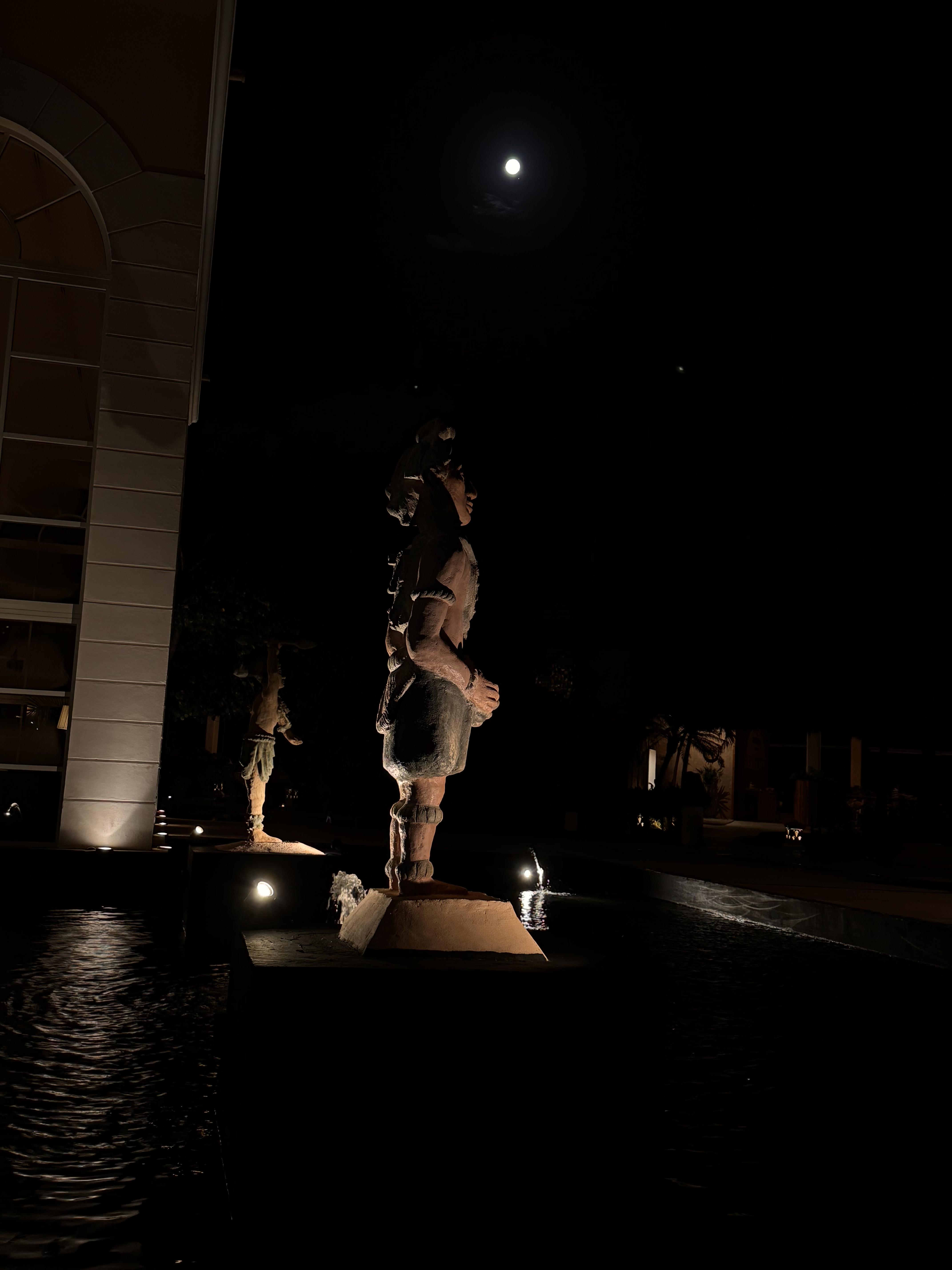 Sculpture of Mayan soldier stands on guard watching over a full moon.